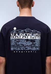 Navy cotton t-shirt featuring a graphic design with mountains, trees, and sun in light blue and white. "NAPAPIJRI" text printed above.