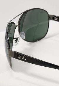 Occhiali da sole Ray-Ban con lenti verdi, montatura e tempie in metallo nero, caratterizzati da un design elegante e un accento in argento con il logo sulla tempia.