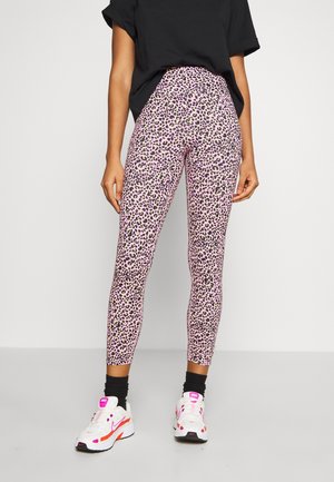 Leggings taille haute de couleur rose avec un motif léopard noir et vert. Associés à des chaussures de sport blanches avec des accents orange et rose.