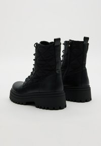 Botas negras con cordones que presentan un upper de tela acolchada, suela de plataforma gruesa y cierre con cremallera lateral para facilitar su uso. Presentan acentos texturizados.