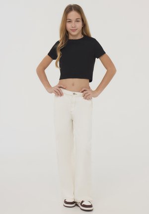 Maglietta nera corta, jeans bianchi a gamba larga e sneakers marroni. L'outfit presenta un design semplice con una vestibilità casual e rilassata.