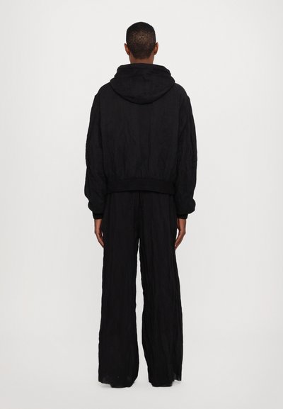 Svart oversized hoodie med texturerad tyg, ribbad nederkant och matchande vida byxor, sedd bakifrån. Enkel design utan synliga mönster.