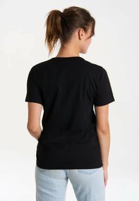 Black cotton t-shirt with short sleeves, round neckline, and clean stitching. Worn with light blue jeans, showing a simple and practical design.