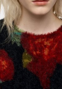 Sweter dziany z okrągłym dekoltem, z czarną bazą i żywymi czerwonymi, żółtymi oraz zielonymi abstrakcyjnymi wzorami. Miękka, puszysta faktura.