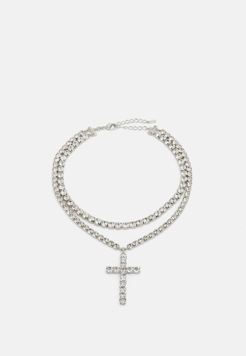 Collier à double chaîne en argent avec strass étincelants et pendentif croix sur fond blanc uni.