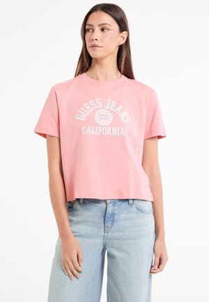 Ružový skrátený tričko z bavlny s bielou potlačou loga "GUESS JEANS CALIFORNIA" na prednej strane a krátkymi rukávmi.