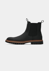 Melni čelzijas zābaki no teksturēta materiāla ar elastīgiem paneļiem un vilkšanas cilpām. Zole ir brūna ar raupju protektoru labākai saķerei.