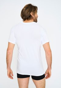 Hvid kortærmet t-shirt lavet af et glat, let materiale. Tætsiddende design med rund halsudskæring og enkel ryg.