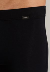 Black stretchy cotton leggings with a smooth texture, featuring a small black label with the brand name "HANRO" on the waistband.