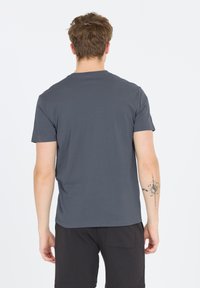 Grå kortärmad bomullströja med rund hals, design på ryggen och mjuk textur. Har en tatuering som syns på vänstra armen.