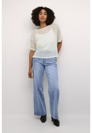 Lichtgroen, gebreid top met korte mouwen en een open breipatroon, gedragen met lichtblauwe wijde jeans en zwarte hoge hakken.