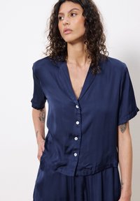 Marineblaue Kurzarm-Hemd mit Knopfleiste, aus einem glatten Stoff gefertigt, mit einem V-Ausschnitt und weißen Knöpfen, in entspannter Passform und weichem Material.