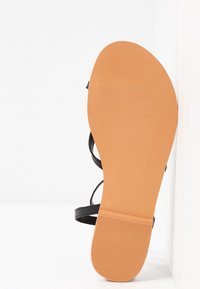 Ploché černé sandály s několika tenkými popruhy. Texturovaná hnědá podrážka se vzorem cikcaku pro lepší uchopení. Minimalistický design, otevřená špička.