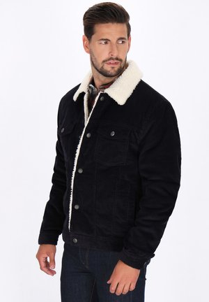 Schwarze Cordjacke mit einem weißen Kunstfellkragen, ausgestattet mit Fronttaschen und Knopfverschluss, strukturierter Stoff, lässige Passform.
