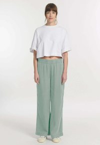 Witte cropped t-shirt met een ronde hals, gecombineerd met lichtgroene wijde broek met elastische tailleband en zonder zichtbare patronen.