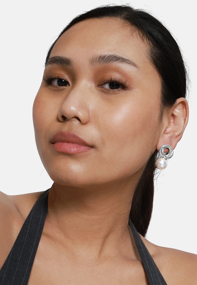 Boucles d'oreilles en argent avec des motifs circulaires entrelacés et un grand accent en perle ; textures lisses et finition polie.