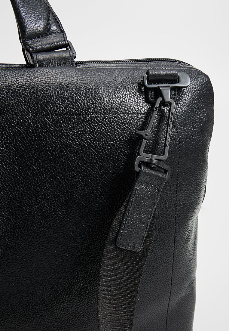 Czarna, teksturowana skórzana torba o gładkim wykończeniu, z metalowym zapięciem i regulowanym paskiem. Smukły, prostokątny design z zamknięciem na zamek błyskawiczny.