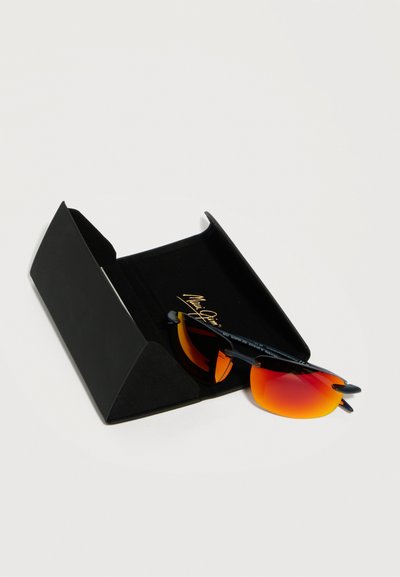 Γυαλιά ηλίου με μαύρο σκελετό και φακούς με πορτοκαλοκόκκινο διαβαθμισμένο χρώμα, τοποθετημένα μέσα σε ανοιχτή μαύρη τριγωνική θήκη γυαλιών ηλίου πάνω σε λευκή επιφάνεια.