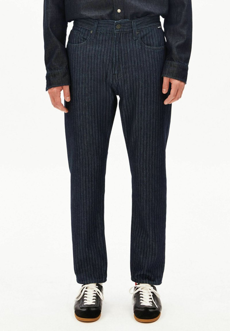 Pantaloni di denim a righe blu scuro con una vestibilità dritta, dotati di tasche frontali, chiusura con bottone e cuciture a contrasto. Abbinati a scarpe nere.