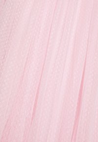 Rosa tyltyg med en mjuk, genomskinlig textur, som har små cirkulära mönster genom hela tyget. Visar en lätt och svävande design.