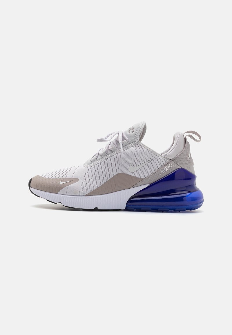 Αθλητικά παπούτσια Nike Air Max 270 σε γκρι και άσπρο, με επάνω μέρος από διχτυωτό υλικό, υφασμάτινες λεπτομέρειες, μοβ αερόσφαιρα και κλείσιμο με κορδόνια.