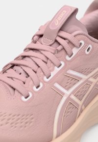 ASICS teka za tek v svetlo roza barvi z teksturiranim zgornjim delom, zaokroženim nosom in nasprotno obarvanimi svetlimi detajli. Ima zavezujoče vezalke in oznako logotipa.