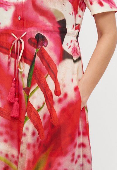Rochie florală în nuanțe de roșu și roz, cu închidere cu nasturi și curea la talie. Are buzunare și accente cu ciucuri pentru un plus de detaliu.