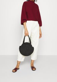 Svart vävd handväska med rund form och två flätade handtag; kombinerad med bordeauxfärgad tröja och vita vida byxor.