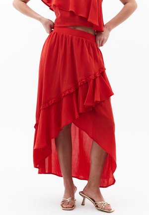 Gonna maxi rossa a strati con fondo arricciato. Realizzata in tessuto leggero, presenta una vita elastica. Abbinata a sandali metallici con cinturini.