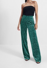 Zielone, szerokie spodnie z weluru o teksturowanej, wzorzystej powierzchni; zestawione z czarną topem bez ramiączek. Gładkie wykończenie, luźny krój.