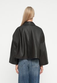 Veste en cuir noir raccourcie avec un large col et des manches surdimensionnées, associée à un jean en denim taille haute. Texture lisse et design minimal.