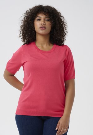 Kurzärmliges korallenfarbenes Shirt aus weichem Strickstoff mit rundem Halsausschnitt, gerippten Bündchen und Saum, kombiniert mit dunkelblauen Jeans.