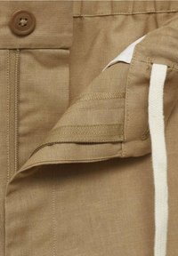 Shorts kaki dotés d'un bouton marron, d'un cordon de serrage, et d'une texture de tissu lisse. Les coutures sont soigneusement réalisées avec des détails subtils.