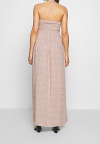 Utan axelband, blommig maxiklänning i dämpade persikotoner, med en rynkad byst, en flödande kjol och subtila vita mönster.