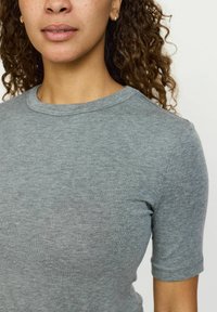 Tricou gri din bumbac cu o textură ribbed, mâneci scurte și decolteu rotund. Materialul pare moale și ușor elastic.