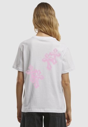 T-shirt en coton blanc avec trois grandes croix décoratives roses au dos. Manches courtes et coupe décontractée.