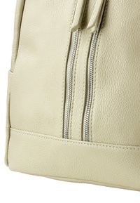 Sac en cuir beige avec deux zippers en métal, surface texturée et base plate. Présente un design simple avec peu d'accents et de coutures.