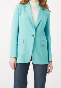 Tyrkysový blazer s přiléhavým střihem, s jedním knoflíkem, klopovými límci a dvěma předními kapsami. Tkanina má hladký, matný povrch.