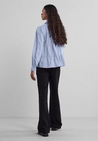 Himmelblaues Peplum-Oberteil mit Puffärmeln, Knopfleiste und gestuftem Design. Kombiniert mit schwarzen, ausgestellten Hosen und Absatzschuhen.