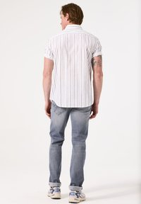 Korte mouwen witte blouse met verticale blauwe strepen, gecombineerd met lichtblauwe jeans en grijze sneakers. De blouse heeft een kraag en een ontspannen pasvorm.