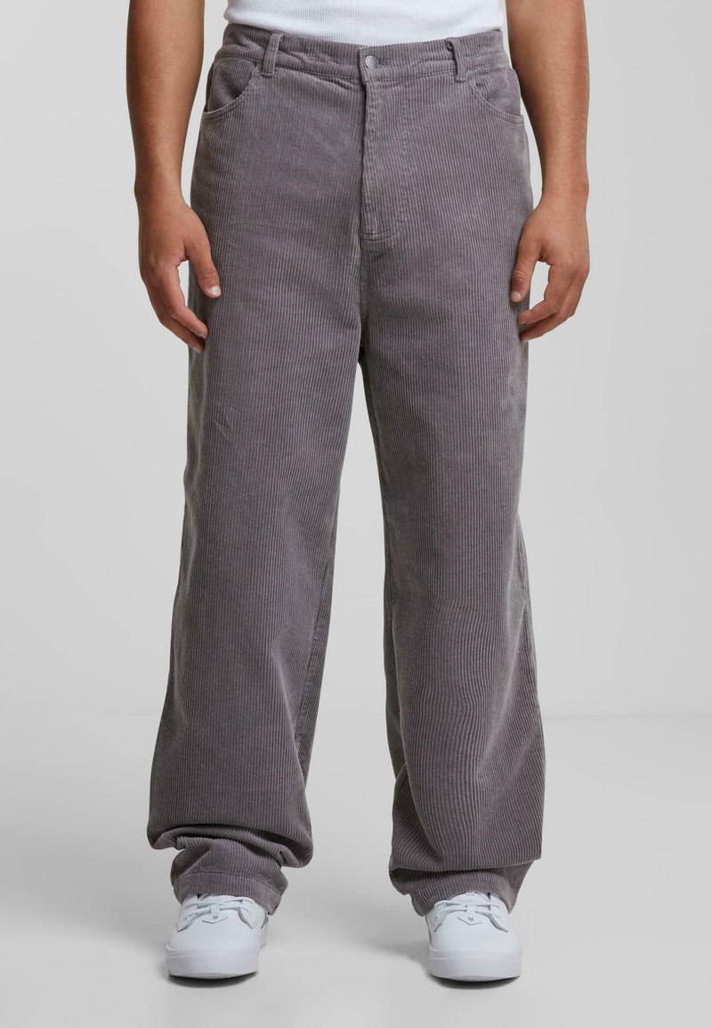 Grijze corduroy broek met een relaxte pasvorm, voorzien van verticale strepen, zijzakken en een rits. Gecombineerd met witte sneakers.