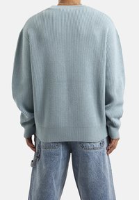 Lichtblauwe geribbelde trui met een losse fit, ronde halslijn en lange mouwen, gecombineerd met vervaagde blauwe denim broek.