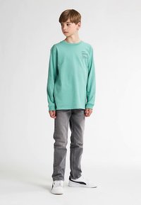 Mintgrünes Langarmshirt mit rundem Ausschnitt und kleinem Aufdruck, kombiniert mit grauen Jeans und weißen Sneakers. Einfaches, bequemes Design mit lockerem Schnitt.