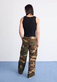 Camiseta de tirantes negra con diseño acanalado, combinada con pantalones cargo de camuflaje que cuentan con bolsillos, en un corte relajado con una textura ligera y tonos terrosos.