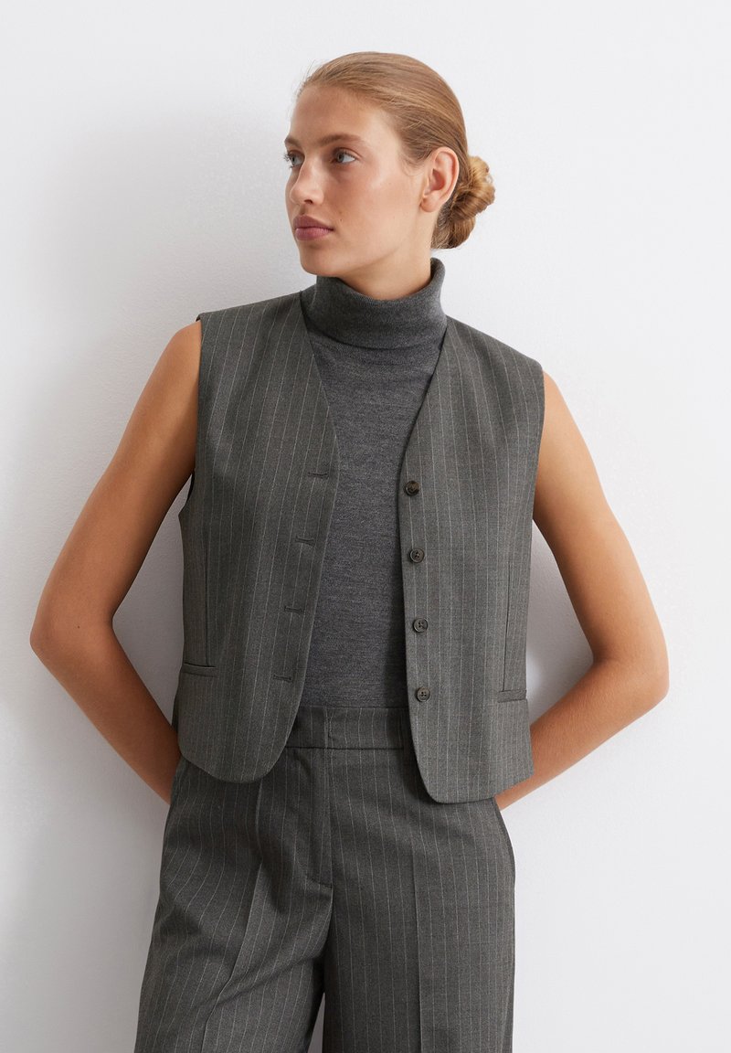 Gray pinstriped vest with a fitted design, sleeveless cut, and button closure, worn over a dark gray turtleneck sweater.