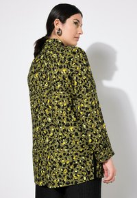 Camisa de estampado de leopardo verde con detalles amarillos, de manga larga, con cuello y aberturas laterales; hecha de una tela suave.