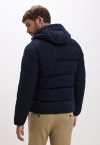 Giacca imbottita blu navy con cappuccio, dotata di polsini a coste e cuciture orizzontali. Il design slim fit si adatta a un aspetto casual.