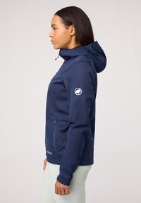 Jūrų pajėgų softshell striukė su priekyje esančiu užtrauktuku, reguliuojama kapišonu ir logotipo pleistru ant kairiojo rankovės. Yra siauras kirpimas ir tekstūruota medžiaga.