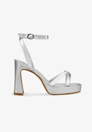 Sandalias plateadas de tacón alto con un acabado metálico brillante, tira en el tobillo y bandas cruzadas en los dedos, presentando un tacón grueso y plataforma.