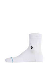 Hvid bomuldsok med ribbet tekstur, ankellængde, med et sort logo på siden og en teal detalje nær tåen.